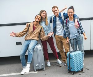 multiethnic-happy-friends-with-travels-bags-gesturing-near-bus-at-street