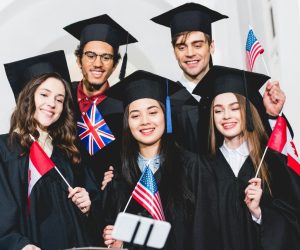 selective-focus-of-cheerful-students-in-graduation-gowns-holding-flags-of-different-countries-and